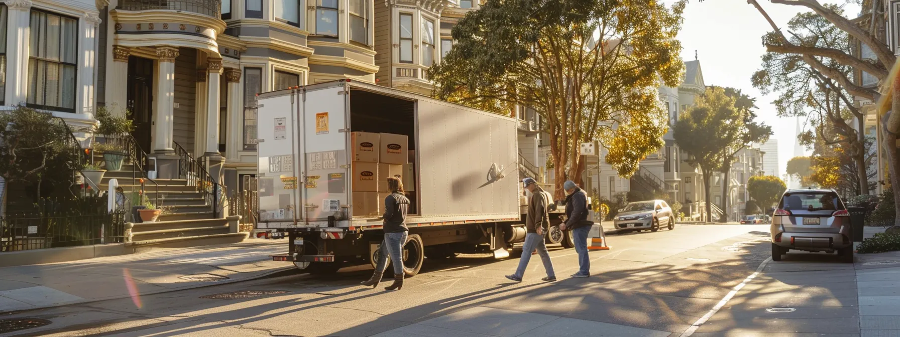 a group of professional movers carefully loading boxes into a moving truck in front of a historic victorian home in downtown san francisco.